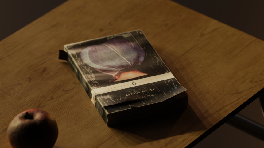 A copy of the book "The Crucible" sitting atop a classroom desk alongside a rotting apple.