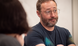A man talks to a student in the foreground. 