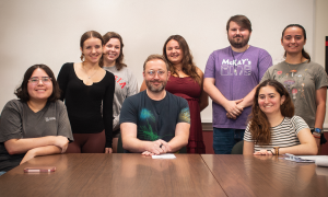 A group of students posing for a photo behind a man. 