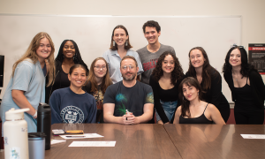 A group of students posing for a photo behind a man. 