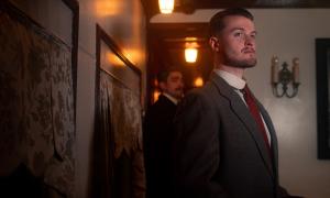 A man in the lounge of a passenger train car while another man stands behind him