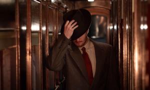 A man putting on a hat while walking in a train corridor