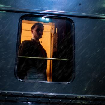 A man looking out of a train with snow blowing by