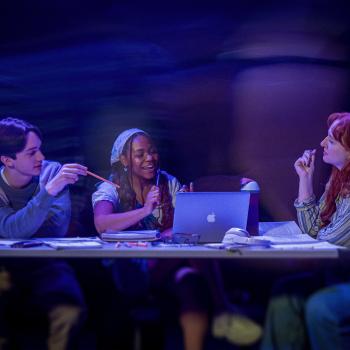 3 students sitting at a table while faded people walk around them